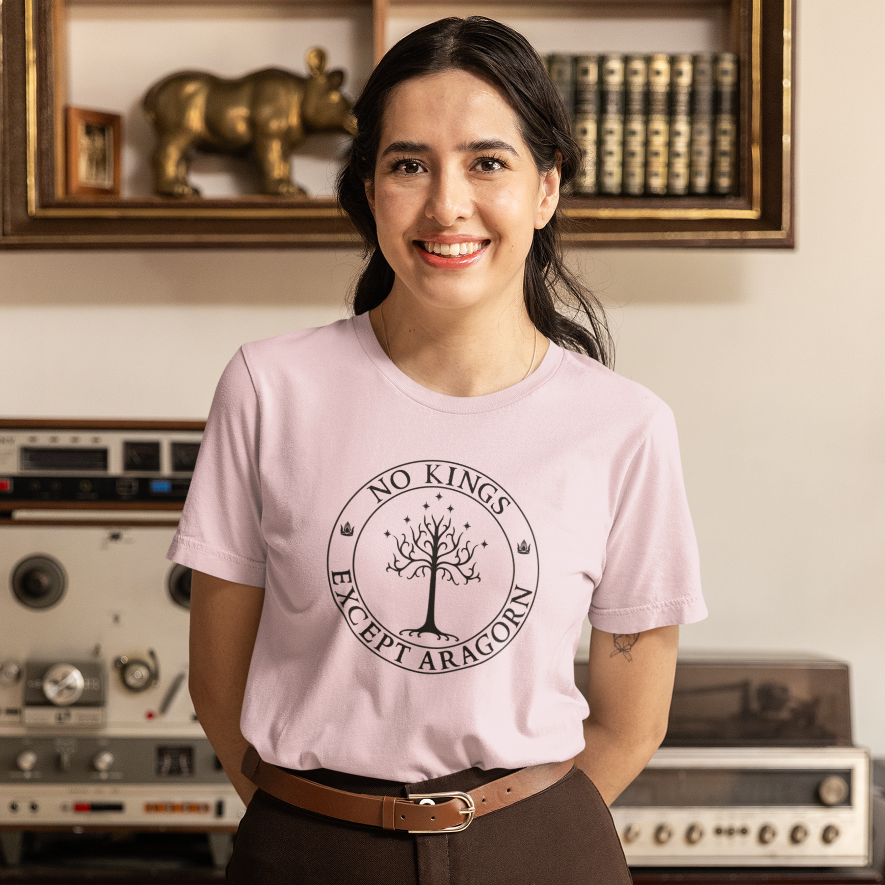 A woman wearing a pink t-shirt with the text "No kings except Aragorn" with a graphic of the white tree of Gondor with seven stars above it and two crowns of the king of Gondor.