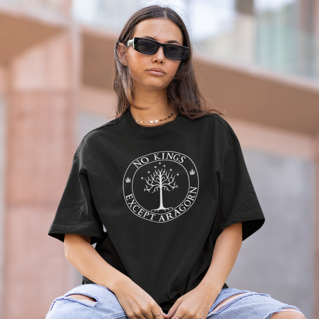 Person wearing a black t-shirt with a logo and ripped jeans sitting on a concrete block outdoors.