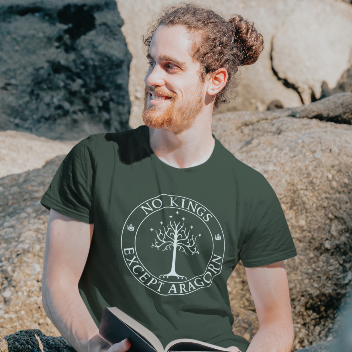 Man sitting on rocks wearing a green t-shirt with a tree design and text, holding a book.